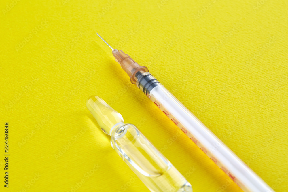 Fototapeta premium Ampoule with medicine and syringe on yellow background