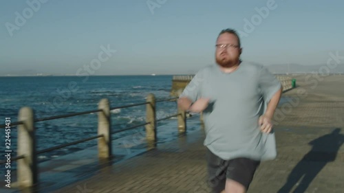 overweight man running intense workout challenge obese caucasian male jogging exercising seaside at sunrise wearing glasses close up