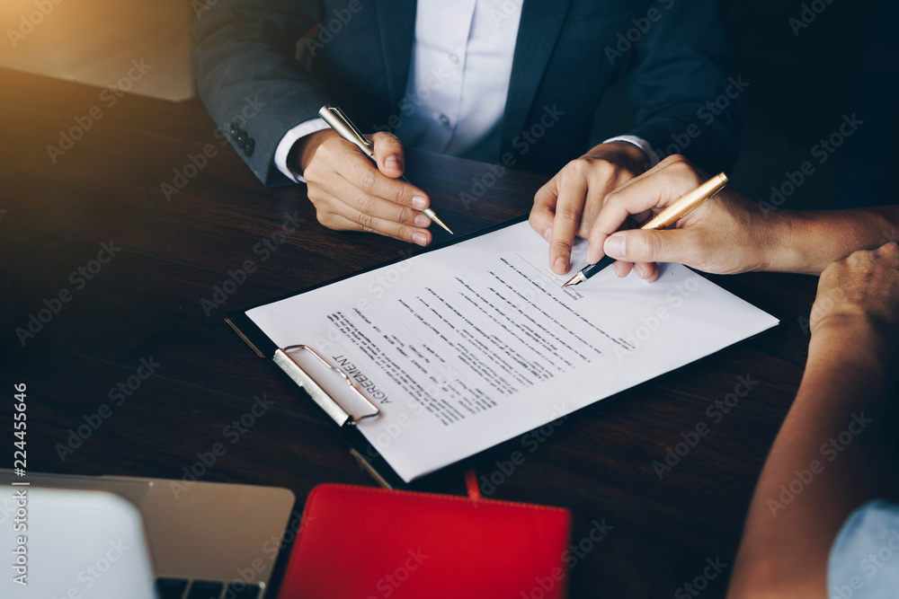 Close up of customer signing a paper document for buying house. Estate agent pointing finger showing where to sign on wooden desk. Real estate, home loan and insurance concept. Close up of customer signing a paper document for buying house. Estate agent pointing finger showing where to sign on wooden desk. Real estate, home loan and insurance concept.