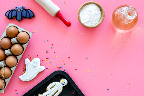 Make halloween gingerbread concept. Icing cookies near rolling pin, baking sheet, eggs, flour on pink background top view copy space