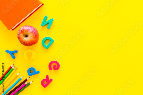 Primary school concept. Letters of english alphabet, apple and color pencils on yellow background top view space for text