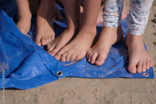 Children with bare feet are standing on a blue synthetic coating on the beach
