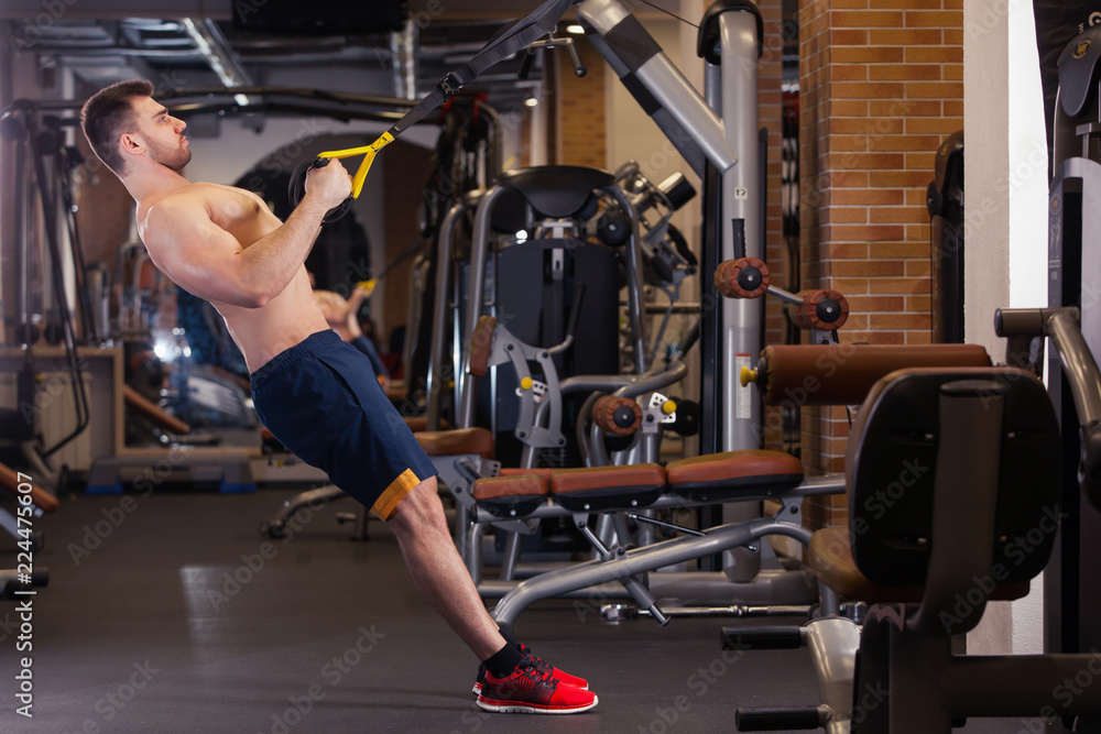 Obraz premium Attractive Man Does Crossfit Push Ups With Trx Fitness Straps In The Gym's Studio