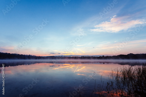 Beautiful, pink violet dawn over the lake. Fog over the lake, the rays of the sun, very dense fog, dawn, the blue sky over the lake, the morning comes, the forest reflects in the water.