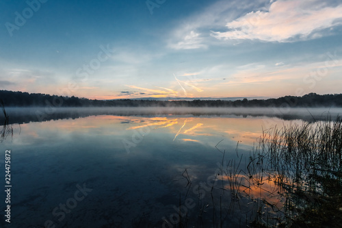 Beautiful  red dawn on the lake. The rays of the sun through the fog. The blue sky over the lake  the morning comes  the sky is reflected in the water.