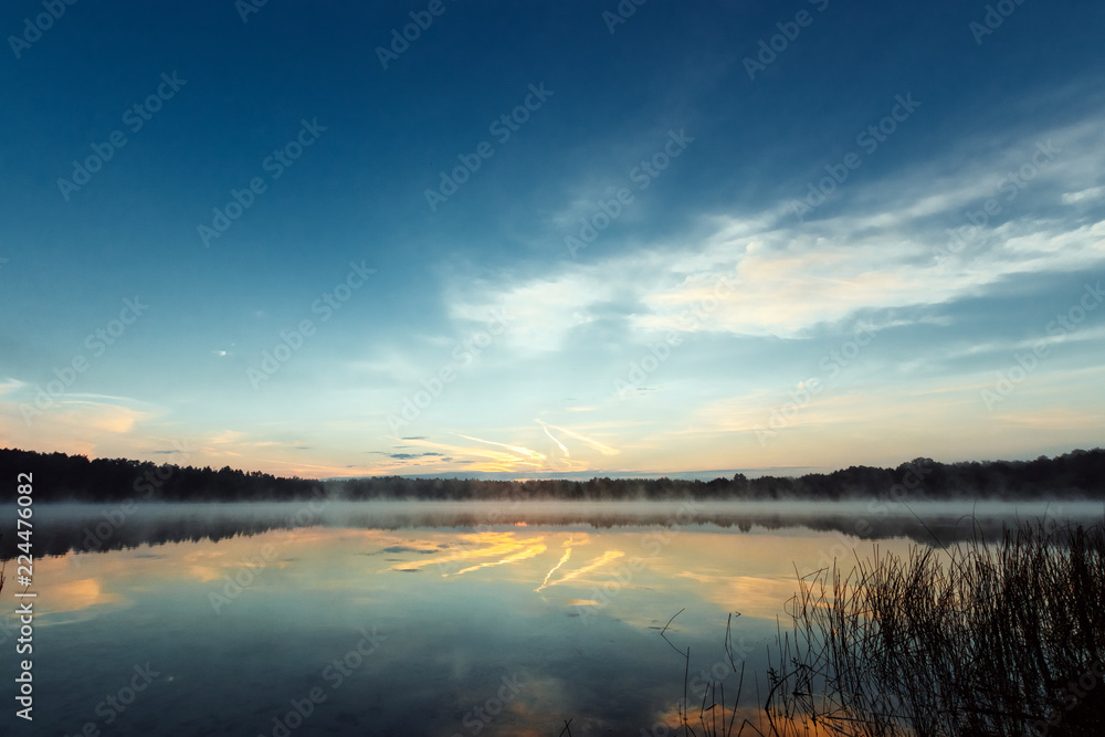 Obraz premium Beautiful, red dawn on the lake. The rays of the sun through the fog. The blue sky over the lake, the morning comes, the sky is reflected in the water.