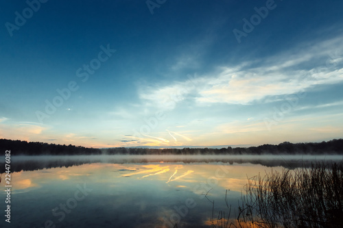 Beautiful, red dawn on the lake. The rays of the sun through the fog. The blue sky over the lake, the morning comes, the sky is reflected in the water.