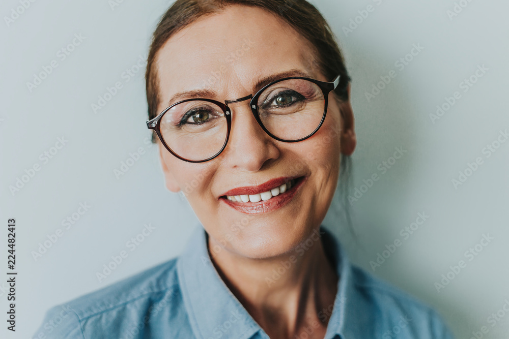 Naklejka premium Beautiful mature woman smiling.Close up portrait of beautiful older woman smiling and standing by wall.Portrait of business woman with glasses smiling.