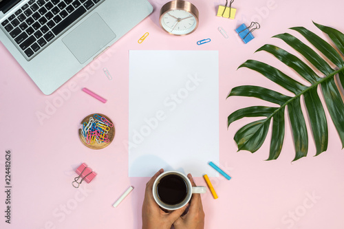 Feminine desk workspace with white paper mockup on pink background. Flat lay, top view.