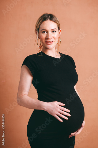 classic portrait of cute beautiful pregnancy with pretty pregnant woman in black dress on a brown background
