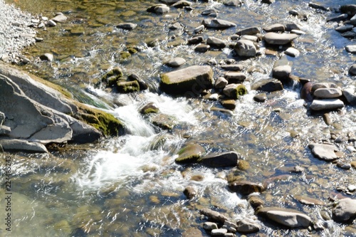 Mountain river running along through rocks with crystal water under the sunshine