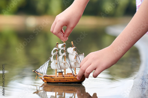 girl playing with a toy sailing ship by the river, hand closeup
