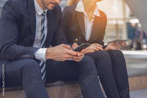 Two business people partners watching media content on a smartphone sitting on a stair outdoor, Man and woman work together looking at mobile phone, Businessman and businesswoman discuss digital data
