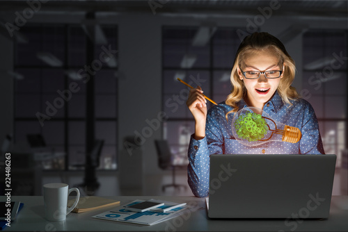 Attractive blonde wearing glasses in dark office using laptop. Mixed media photo