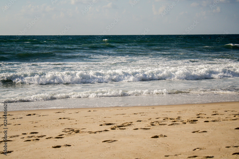 Seascape, blue waves with white foam on the beach with golden sand under a blue sky Seascape, blue waves with white foam on the beach with golden sand under a blue sky