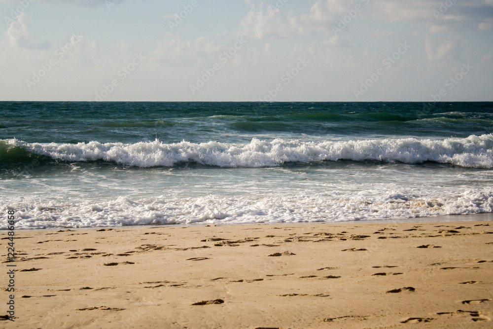 Seascape, blue waves with white foam on the beach with golden sand under a blue sky Seascape, blue waves with white foam on the beach with golden sand under a blue sky