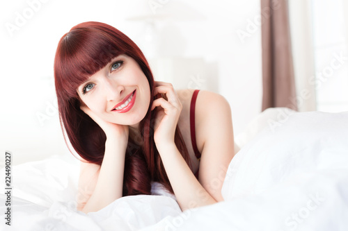 Beautiful smiling young woman lying on bed at home