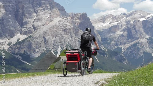 Man riding mountain bike with his child in a bicycle trailer in the mountains, Dolomites, Italy