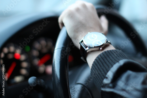 young man wearing leather jacket and wrist watches driving behind a wheel