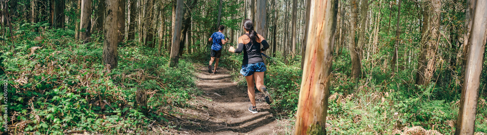 Young woman and man participating in a trail race through the forest Young woman and man participating in a trail race through the forest