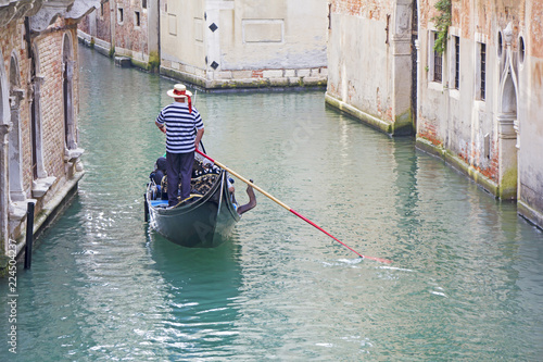 Venetian gondolier in the gondola is transported tourists through canal waters of Venice Italy