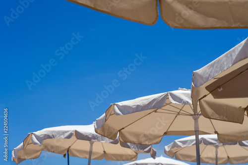 View from below of blue skies on a beach with parasols over deck chairs.