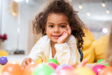 smiling african american kid lying on carpet with toys and looking at camera in kindergarten
