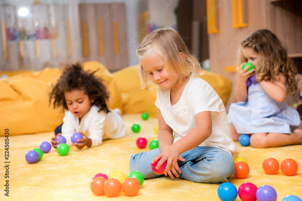 Fototapeta premium adorable multicultural kids playing with colored balls on floor in kindergarten
