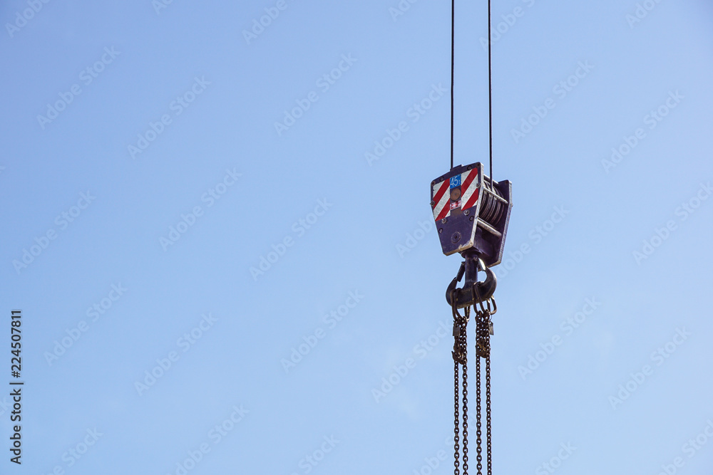 Crane hook with red and white stripes hanging, blue sky in background . Crane hook with red and white stripes hanging, blue sky in background .