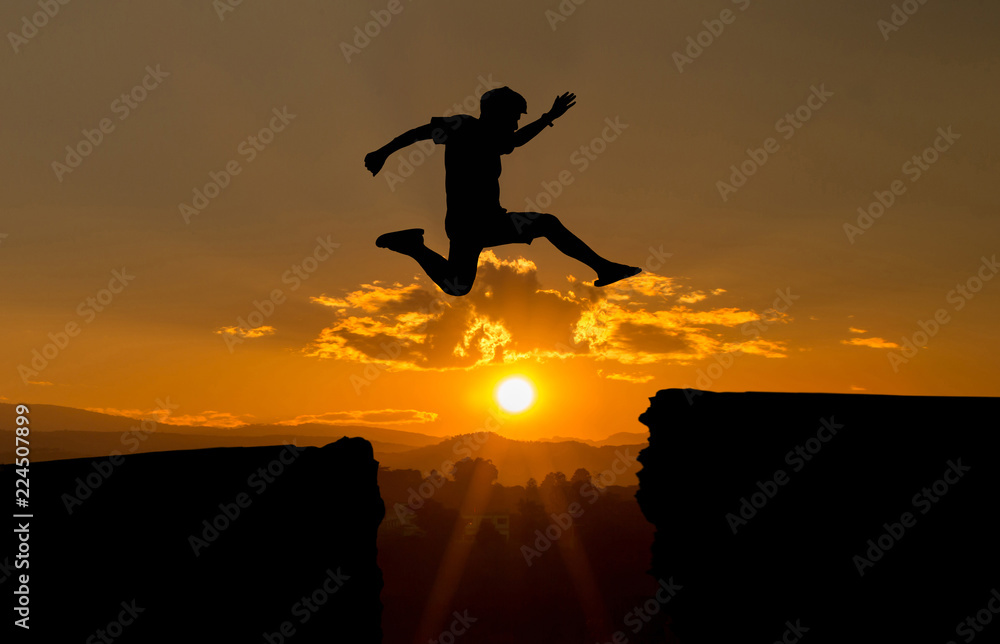 young man jump over the sun and through on the gap of hill silhouette evening colorful sky.image for spirit brave concept.man is representative of success in the past and gold for the future in 2019