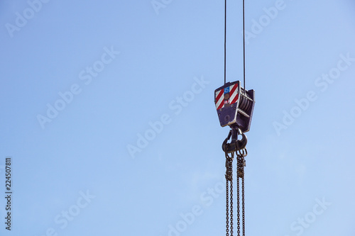 Crane hook with red and white stripes hanging, blue sky in background .