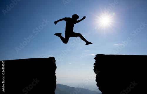 man jump over through on the gap of hill silhouette light, blue sky and sun on background.image for spirit and brave concept.spirit man is representative of success in the past and gold for the future