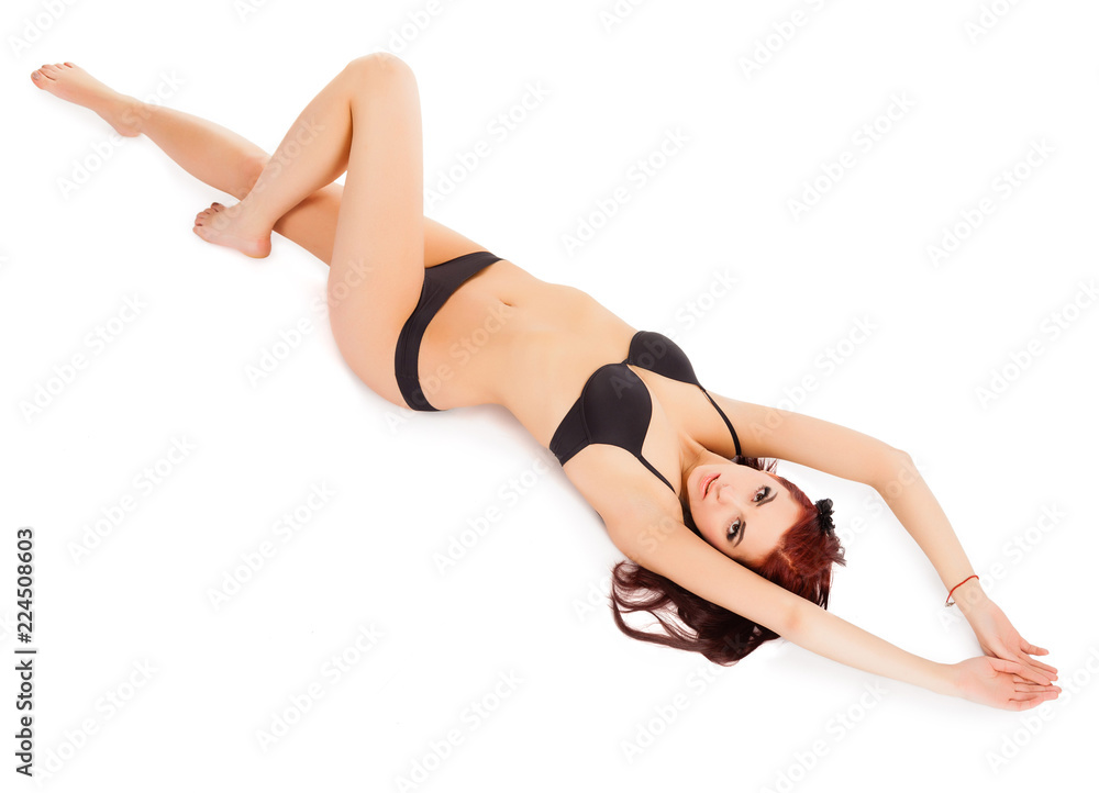 Beautiful young woman in black bikini lying on back isolated on white