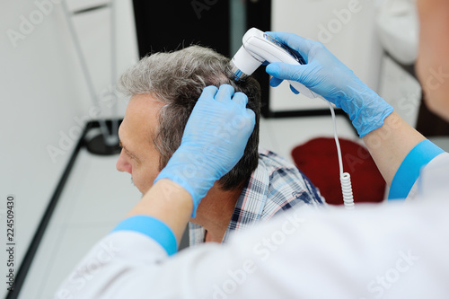 baldness. doctor examines an elderly man hair using special equipment - trihoskopa