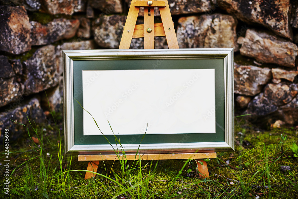 Easel staying om grass and moss near ancient stone walll with copy space