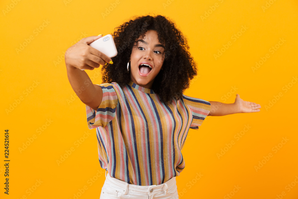 African woman posing isolated over yellow background take a selfie by mobile phone. African woman posing isolated over yellow background take a selfie by mobile phone.