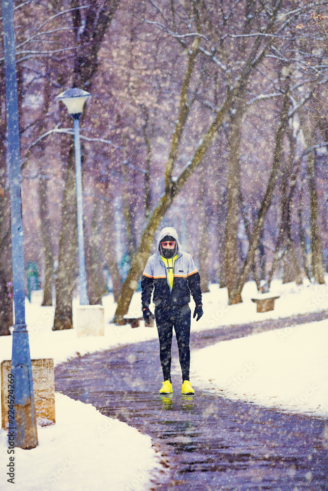 Man jogging in snowy park and cold weather.