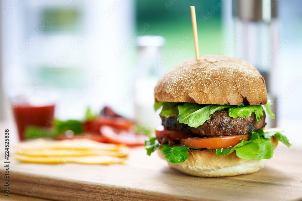 A beef burger in a crusty bun with lettuce and tomatoes on a cho