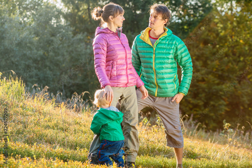 Fototapeta premium Family, childhood, fatherhood, leisure and people concept - happy father, mother and little toddler son playing and having fun outdoors over nature park fall autunmn background.