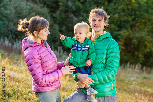 Family, childhood, fatherhood, leisure and people concept - happy father, mother and little toddler son playing and having fun outdoors over nature park fall autunmn background. photo