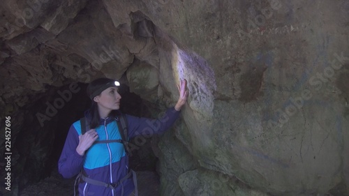 portrait of a tourist girl with a backpack in the cave touches the wall photo