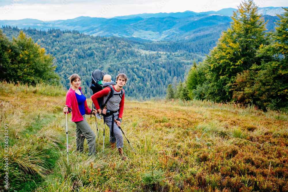 Couple hiking with baby boy travelling in backpack. Hikers family, adventure with child on summer family trip in mountains. Vacations journey with toddler carried on back, weekend travel concept.