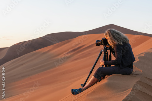 Africa, Namibia, Namib desert, Naukluft National Park, female photographer photographing at early morning light, sitting on sand dune photo
