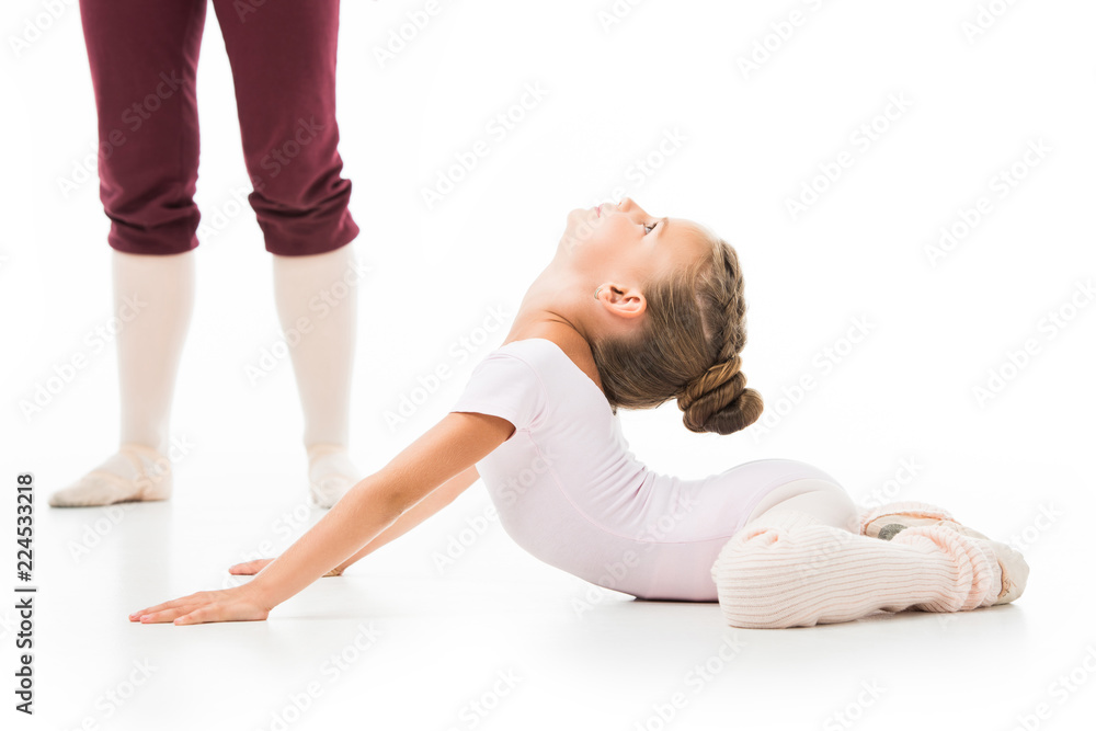cropped image of female trainer in pointe shoes standing near little ballerina while she stretching isolated on white background