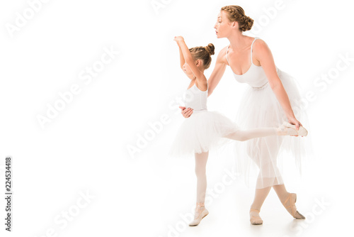side view of adult female trainer in tutu helping little ballerina exercising isolated on white background
