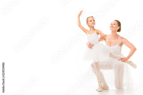 smiling adult female coach helping little ballerina exercising isolated on white background