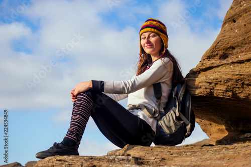 Beautiful slim and sporty young tourist woman in a funny hat from Nepal wool yak sitting and have rest climbing big rock climbs on boulders canyon stones sky background