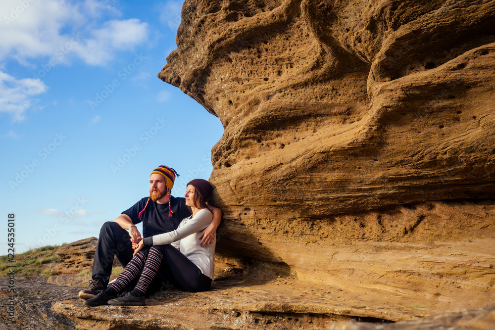couple in love on a canyon trip. Man brave red-haired beard climbing bouldering stone rock tourist climbs up with backpack in a black T-shirt and a funny hat made of wool of yak from Nepal and woman