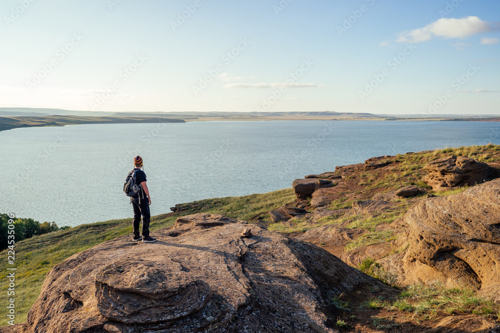 man travel blogger in a funny hat from Nepal mountain Hiker with backpack hike walking on orange huge stones landscape lake and hills