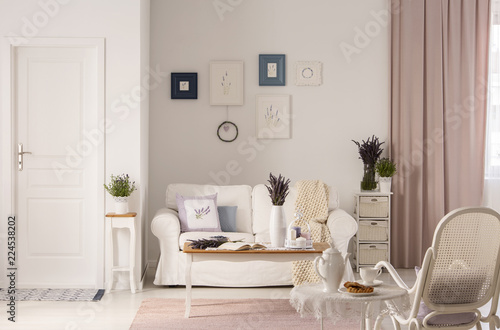 Flowers on table in front of white sofa in pink living room interior with door and armchair. Real photo